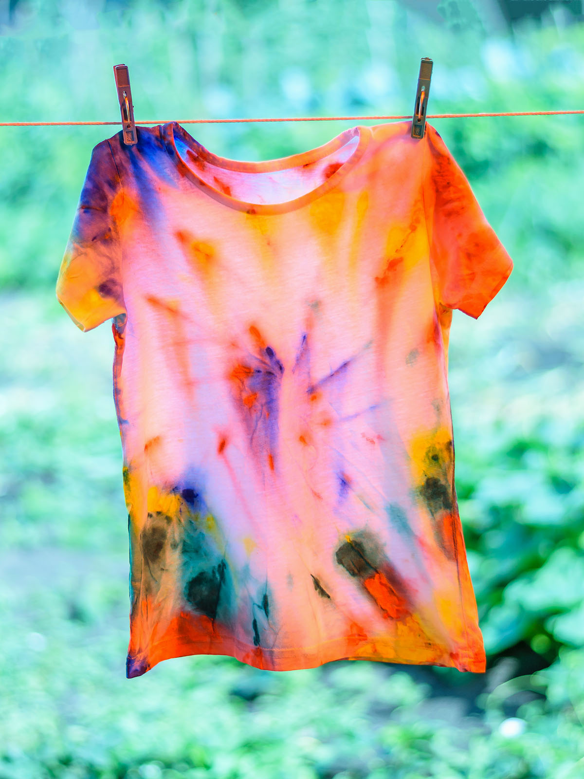 shirt painted in tie dye style is dried on a rope.